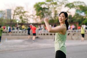 kvinna joggare. passa ung asiatisk kvinna med grön sportkläder aerobics dansa övning i parkera och njuter en friska utomhus. kondition löpare flicka i offentlig parkera. wellness varelse begrepp foto