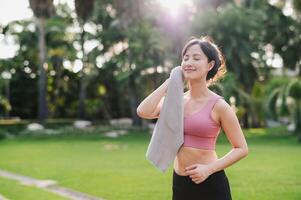 självsäker 30s asiatisk kvinna i rosa sportkläder våtservetter henne kind efter solnedgång träna i natur. fångar skönhet av friska livsstil och perfekt för några projekt främja kondition, hälsa, eller motivering. foto