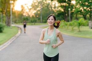 passa asiatisk ung kvinna joggning i parkera leende Lycklig löpning och njuter en friska utomhus- livsstil. kvinna joggare. kondition löpare flicka i offentlig parkera. friska livsstil och wellness varelse begrepp foto