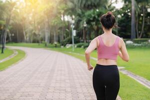 kvinna joggare. tillbaka perspektiv porträtt av ung asiatisk kvinna bär rosa sportkläder löpning i offentlig parkera. sjukvård wellness begrepp. foto