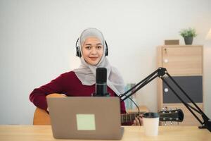 muslim islam kvinna bär hijab leva strömning prestanda spelar gitarr och sjunga en låt. asiatisk kvinnor undervisning gitarr och sång uppkopplad. musiker inspelning musik med bärbar dator spelar akustisk gitarr. foto