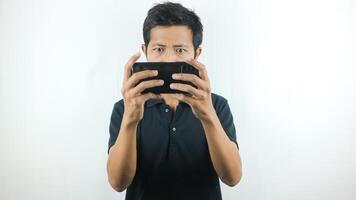 asiatisk man med en allvarlig uttryck är spelar en spel på hans cell telefon. foto