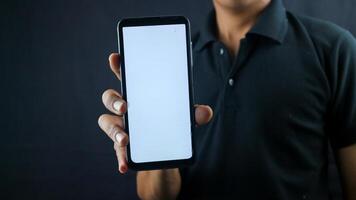asiatisk man innehav stor smartphone med tom skärm i hand, som visar stänga till kamera och pekande på enhet. grej med tömma fri Plats för falsk upp, baner foto