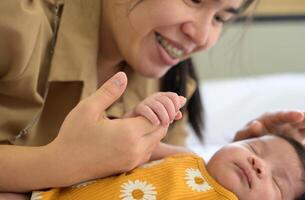 nyfödd bebis flicka innehav mor hand. leende mamma och barn på vit säng. foto