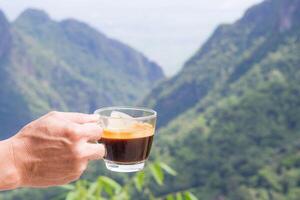 närbild av en man hand innehav en kopp av kaffe med en skön naturskön se av berg. begrepp av resa och avslappning foto