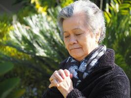 porträtt av ett äldre kvinna stående och ögon stängd bön- medan stående i de trädgård foto