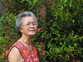 asiatisk äldre kvinna ser bort och leende medan stående i en trädgård foto