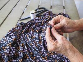 närbild av gammal kvinna händer använder sig av nål och tråd till laga trasa. foto