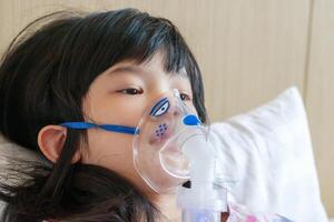 sjuk liten asiatisk flicka inandning med nebulisator för respiratorisk behandling foto