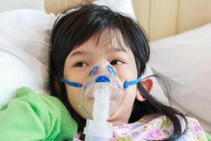 sjuk liten asiatisk flicka inandning med nebulisator för respiratorisk behandling foto