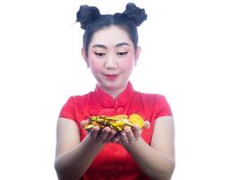 porträtt asiatisk ung, kvinna röd klänning traditionell cheongsam håller ett guldmynt på den vita bakgrunden foto