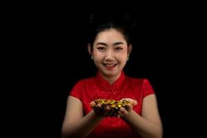 porträtt asiatisk ung, kvinna röd klänning traditionell cheongsam som håller ett guldmynt på svart bakgrund, foto