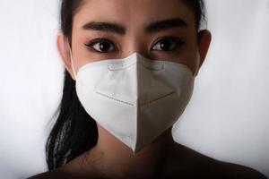 närbild av ung asiatisk kvinna som tar på sig en medicinsk mask n95 för att skydda mot luftburna luftvägssjukdomar som influensa covid-19 pm2.5 damm och smog på grå bakgrund, säkerhetsvirusinfektion koncept foto