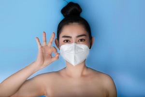 närbild av en kvinna som sätter på sig en respirator n95-mask för att skydda mot luftburna luftvägssjukdomar som influensa covid-19 corona pm2.5 damm och smog, kvinnlig tummen upp gest med handen visar ok tecken