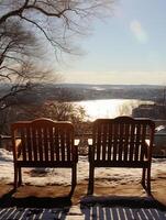 ai genererad två trä- stolar på en snöig kulle utsikt en sjö. vinter- landskap foto