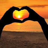 två händer av älskare på bakgrund av solnedgången på havet foto