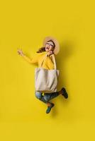 porträtt av en upphetsad vacker flicka som bär klänning och solglasögon som håller shoppingkassar. glad ung kvinna med handväska på gul bakgrund. shopaholic shopping mode. foto
