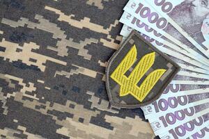 ukrainska armén symbol och knippa av hryvnian räkningar på militär enhetlig. betalningar till soldater av de ukrainska armé, löner till de militär foto