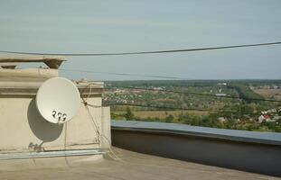 vit satellit maträtt med tre omvandlare monterad på bosatt byggnad taket betong vägg. satellit tv foto