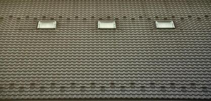 de textur av de tak med en tak tillverkad av metall, täckt med droppar från de regn. flera Ruta fönster är byggd in i de tak foto