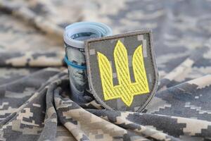 ukrainska armén symbol och knippa av dollar räkningar på militär enhetlig. betalningar till soldater av de ukrainska armén från förenad stater, löner till de militär. krig Stöd foto