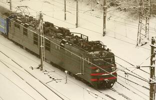 en lång tåg av passagerare bilar är rör på sig längs de järnväg Spår. järnväg landskap i vinter- efter snöfall foto