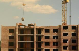 se av en stor konstruktion webbplats med byggnader under konstruktion och flera våningar bostads- hem. torn kranar i verkan på blå himmel bakgrund. hus renovering begrepp foto