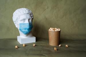 de begrepp av matning en person i en medicinsk mask med mat, spill mat i främre av de ansikte i en mask, häller popcorn från en burk på de tabell, plåster huvud i en skyddande mask, karantän, konst foto