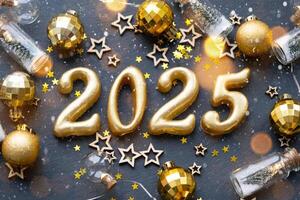 de gyllene siffror 2025 tillverkad av ljus på en svart sten skiffer bakgrund är dekorerad med en festlig dekor av stjärnor, paljetter, gran grenar, bollar och girlanger. hälsning kort, Lycklig ny år. foto