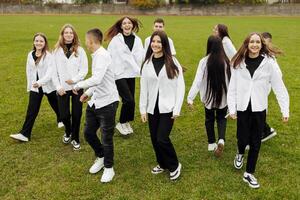 en grupp av många Lycklig tonåringar klädd i de samma utrusta har roligt och Framställ i en stadion nära en högskola. begrepp av vänskap, stunder av lycka. skola vänskap foto