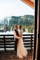 de brudgum omfamnar de brud mot de bakgrund av snötäckt berg. en bröllop par är fira en bröllop i de bergen i vinter. foto