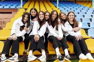 en grupp av många Lycklig tonåringar klädd i de samma utrusta har roligt och Framställ i en stadion nära en högskola. begrepp av vänskap, stunder av lycka. skola vänskap foto