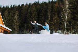 ung man och kvinna löpning liggande på snö, skrattande, lurar runt om, har roligt spelar snöbollar. europeisk vinter- bröllop foto