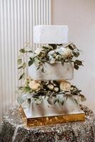 en stor lyxig flerdelad bröllop kaka är dekorerad med färsk blommor av vit ro och eukalyptus löv i de bankett hall. bröllop efterrätt under de kväll ljus. bröllop dekor. foto