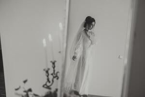 porträtt av en lyxig brud i budoar stil nära en spegel med reflexion. framställning de brud för de bröllop i de morgon- i en vit morgonrock. foto