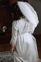 de morgon- av de brud, en kvinna bär en vit silke morgonrock innehar en bröllop bukett. Foto från de tillbaka med de inskrift brud