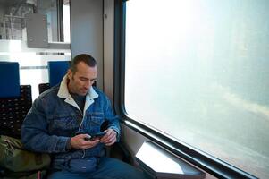 caucasian man pendlare använder sig av smartphone, kontroll mobil app, planera rutt medan reser förbi bekväm stad tåg. foto