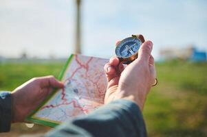 manlig hand innehar kompass med magnetisk pil som visar norr riktning, över en Karta medan upptäcker en ny resa destination foto