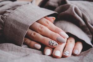 kvinnas hand med en skön ovalformad manikyr. höst trend, beige Färg putsning med leopard mönster på naglar med gel putsa, schellack. foto