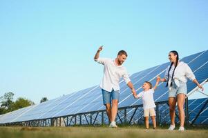 ung familj av tre är hukande nära solceller sol- panel, liten pojke och föräldrar. modern familj begrepp. de begrepp av grön energi foto