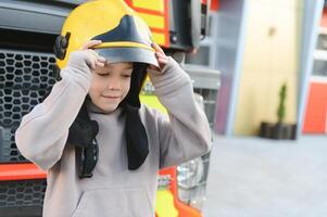 barn, söt pojke, klädd i brand figurer torkdukar i en brand station med brand lastbil, childs dröm foto