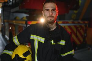 brandman i skyddande enhetlig stående nära brand motor på station foto