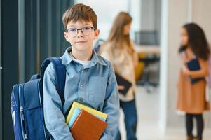 Lycklig söt duktig pojke i glasögon med skola väska och bok i hans hand foto