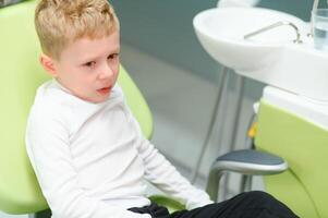 rädd rödhårig pojke gråt på reception på tandläkare i dental stol. pediatrisk tandvård foto