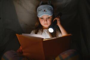 en Söt liten flicka läsning en bok på de golv under de lampa. barn och utbildning foto