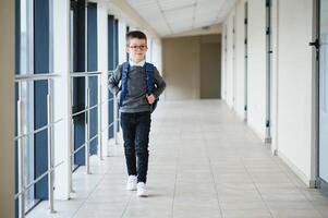 Lycklig söt duktig pojke i glasögon med skola väska och bok i hans hand. först tid till skola. tillbaka till skola. foto