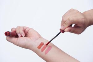 stänga upp kvinna hand är testning läpp glans annorlunda färger, tillämpa på henne ärm. läppstift färgrutor på hand för färger testa eller kosmetisk allergi testa. göra upp Utrustning eller verktyg. foto