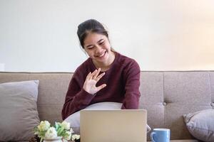 avslappnad ung asiatisk kvinna njuter avslappning på en bekväm soffa på Hem. de skön flicka lugnt slappnar av och andas färsk luft i de hus. Kolla på bio och social nätverk. foto