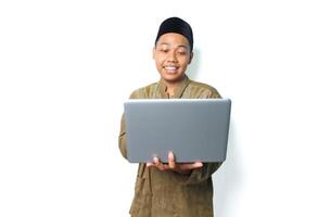 glad asiatisk muslim man bär islamic klänning innehav bärbar dator isolerat på vit bakgrund foto