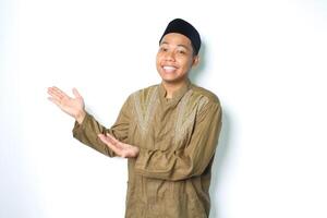 Lycklig asiatisk muslim man bär koko kläder presenter till bredvid med öppen palmer isolerat på vit bakgrund foto